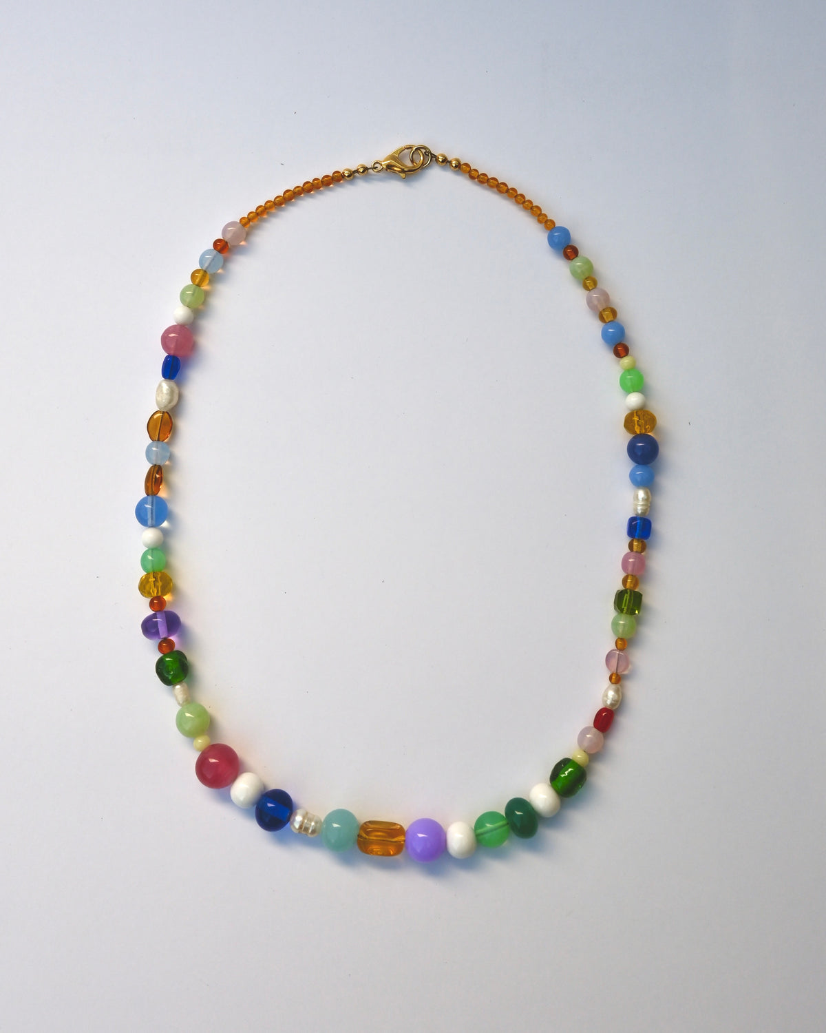 A colorful beaded necklace with a mix of translucent and opaque beads in various colors, featuring a gold clasp, displayed on a light blue background.