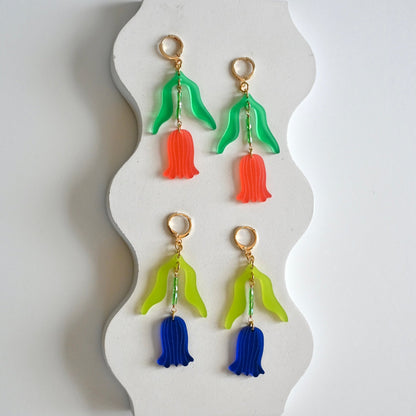 A collection of art nouveau inspired tulip earrings displayed on a white stand, with gold plated huggie hoops and multicolored acrylic and glass beads.